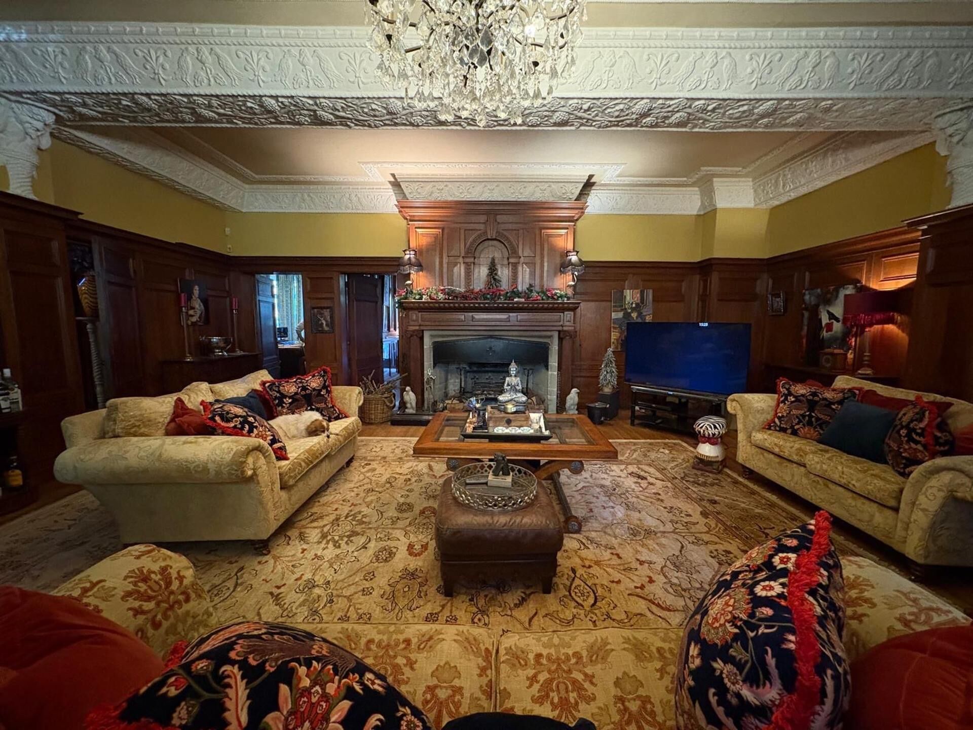 A traditional living room with two sofas, a fireplace, a television, and a chandelier.