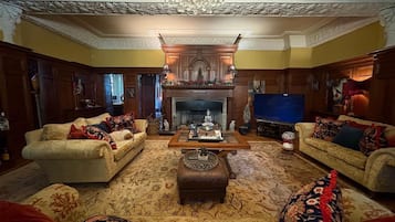 A traditional living room with two sofas, a fireplace, a television, and a chandelier.