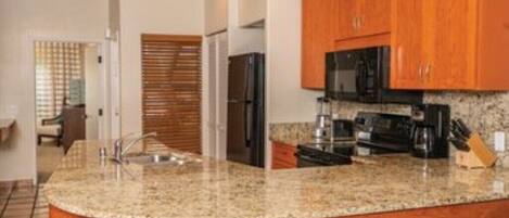 A kitchen with granite countertops, wooden cabinets, a stainless steel refrigerator, and a black microwave.