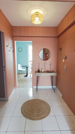 A hallway with a round rug, a wall-mounted mirror, and a door leading to a room with a blue wall and a white chair. - Property - 4 bedrooms - 8 guests (Perpignan)