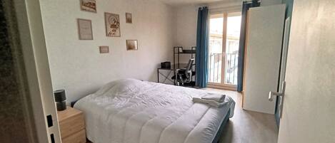 Ein Schlafzimmer mit einem Bett, einem Schreibtisch und einem Stuhl. An den Wänden befinden sich Bilder und ein Fenster mit Vorhängen.