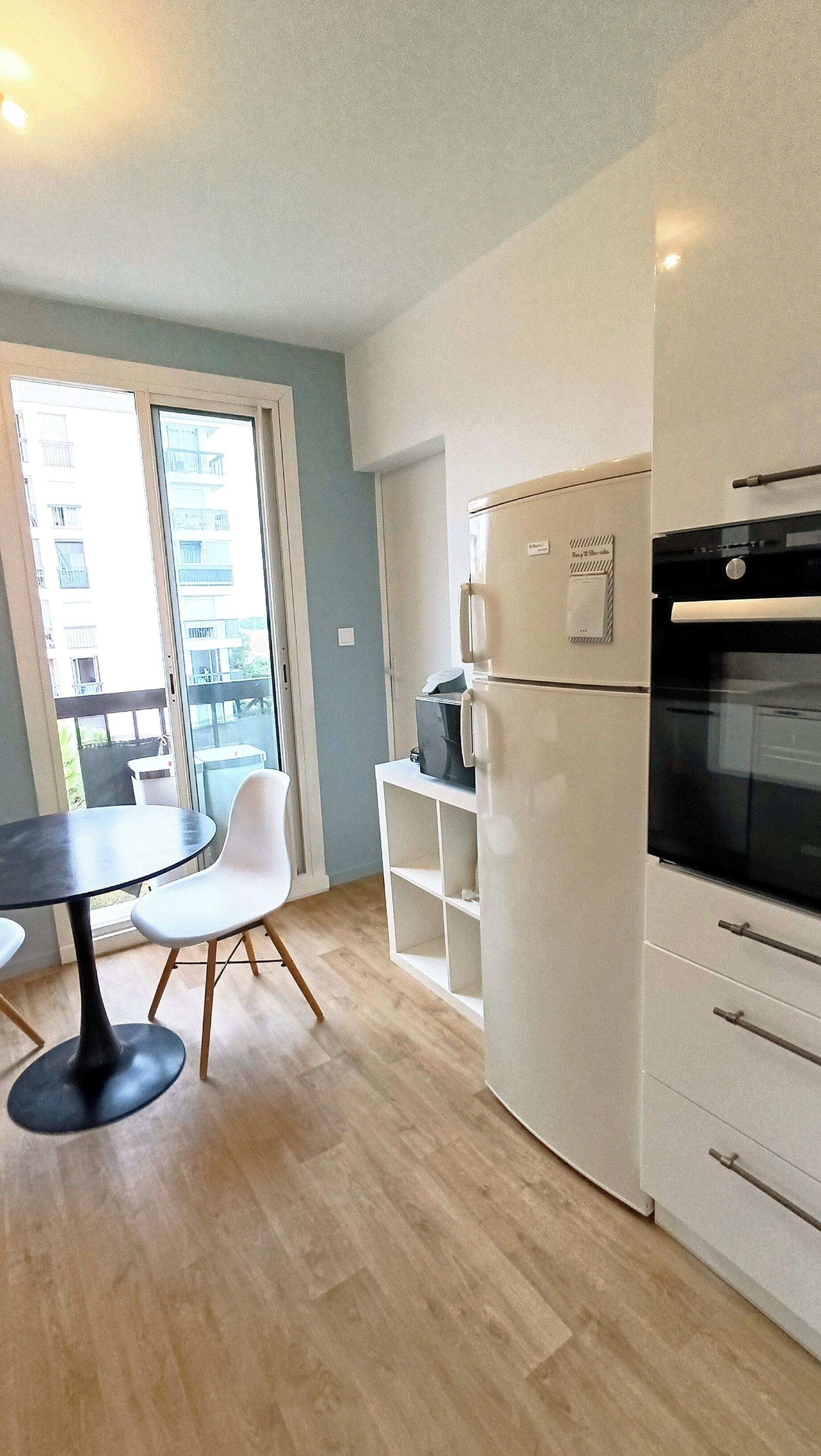 Une cuisine de taille réduite équipée d’un réfrigérateur, d’un four et d’une petite table à manger avec des chaises.