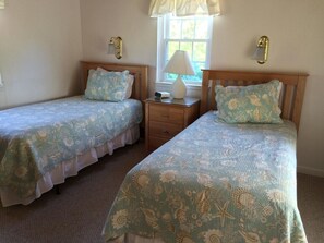 A room with two single beds, each with a matching headboard and pillow, a bedside table with a lamp, and a window with curtains. - Charming Nantucket Cottage w/ Private Beach Access - 50%! (Nantucket)