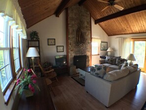Uma sala de estar acolhedora com lareira de pedra, vigas de madeira e um sofá confortável.
