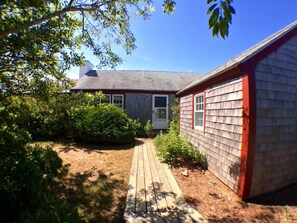 Um deck de madeira que leva a uma casa com telhado cinzento e fachada vermelha.