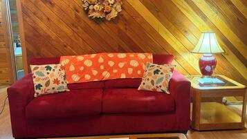 A red sofa with patterned cushions, a glass-top coffee table with magazines and a menu, and a wooden wall with a decorative wreath.