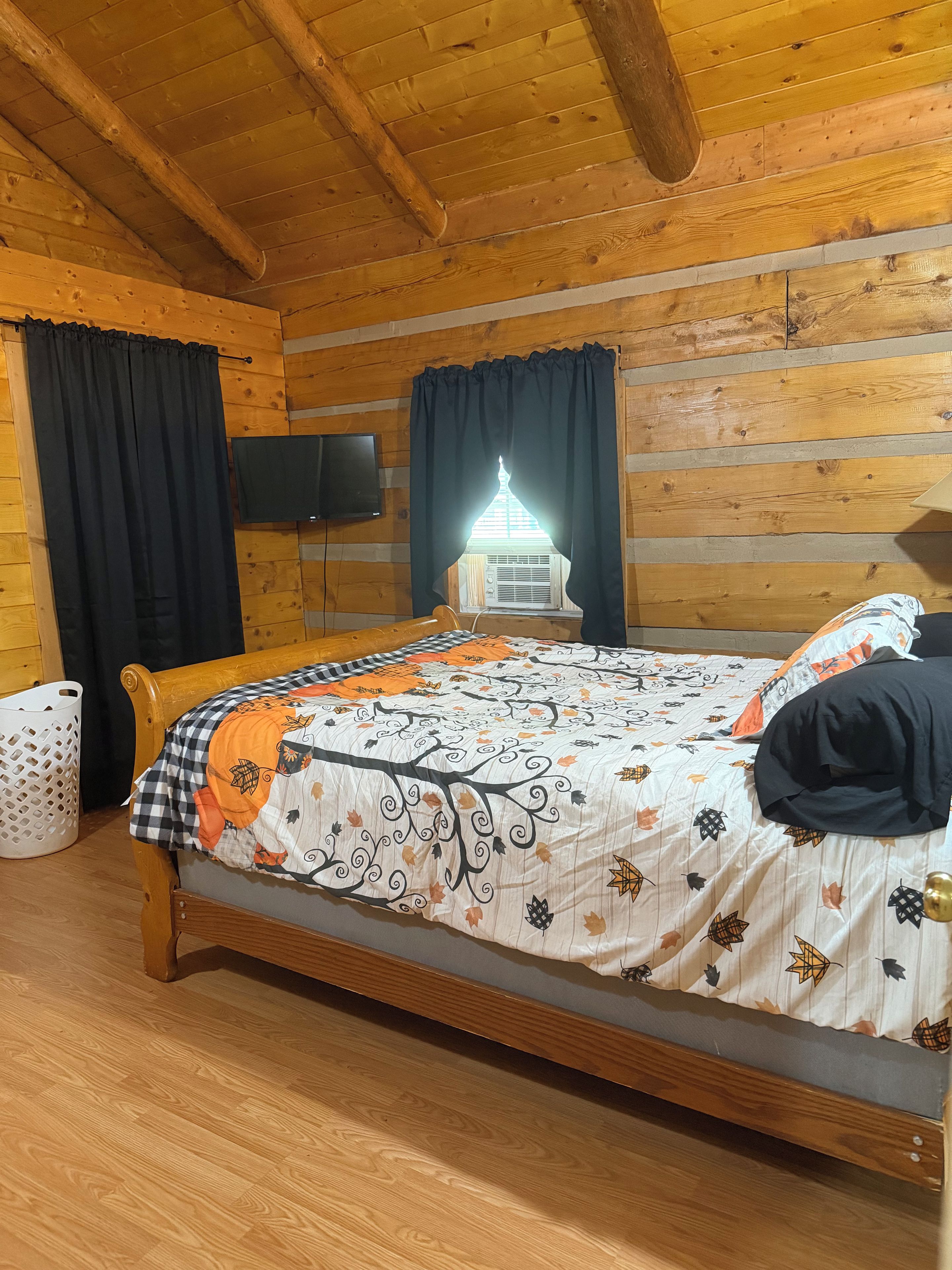 Une chambre dans un chalet en bois, avec un lit, une télévision et une fenêtre avec des rideaux.