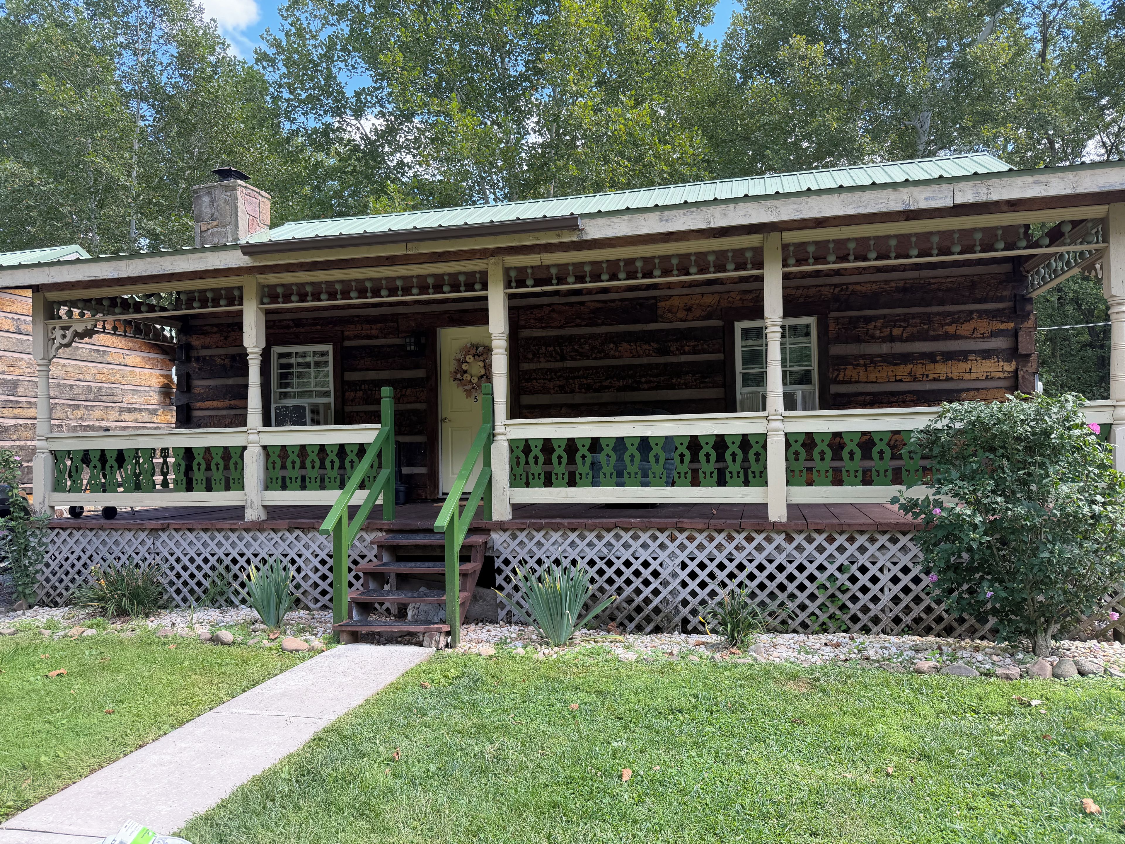 A log cabin with a porch, a chimney, and a small garden.
