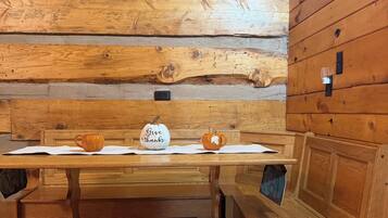 A wooden table with two mugs and a sign that says 'Give thanks' in a cabin-style room with wooden walls and benches.
