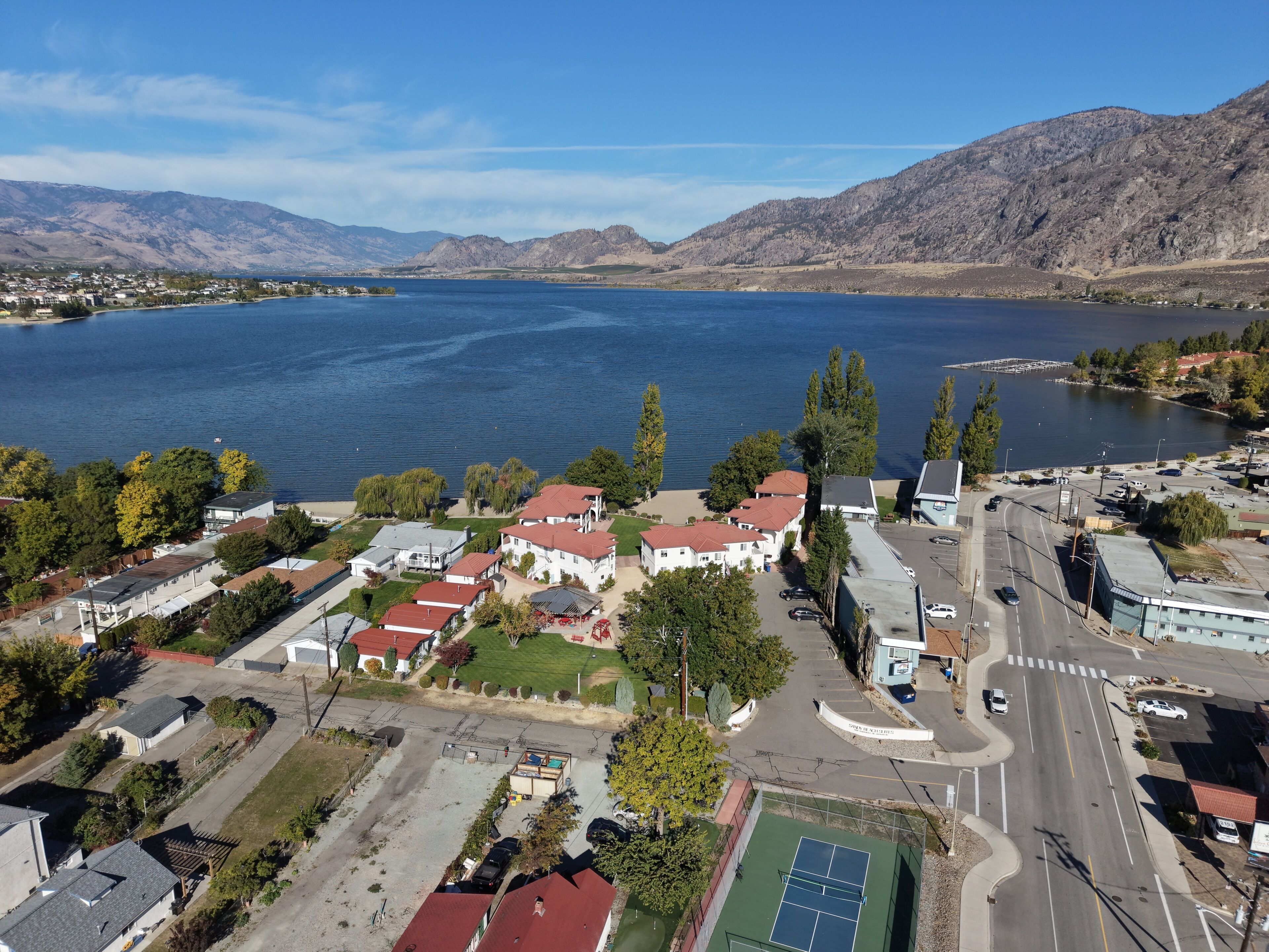 A residential area with houses, a tennis court, and a road with vehicles.