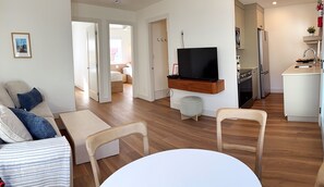 Ein modernes Wohnzimmer mit einer Couch, Sesseln, einem Fernseher und einem Esstisch.