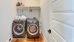 Une buanderie équipée de deux machines à laver à chargement frontal, d’une étagère avec des serviettes pliées et d’une porte dotée d’une poignée.