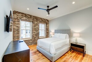Un dormitorio con pared de ladrillo decorativa, una cama, una mesita de noche, un escritorio y un ventilador de techo.