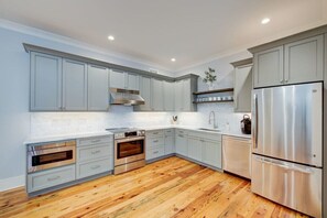 A modern kitchen with grey cabinets, stainless steel appliances, and a wooden floor. - Deluxe Two Bedroom Suite - Steps to King Street (Charleston)