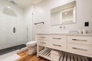Un baño moderno con cabina de ducha de vidrio, inodoro blanco, tocador con cajones y un espejo.