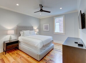 A bedroom with a bed, nightstands, a ceiling fan, a window, and a TV stand. - Deluxe Two Bedroom Suite - Steps to King Street (Charleston)