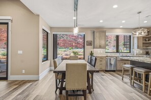 A modern kitchen with a dining area, large windows with a view of red rock formations, and a hanging light fixture.
