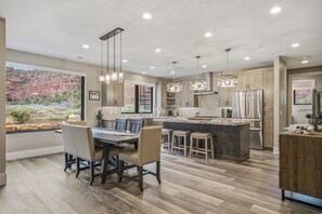 A modern kitchen with a central island, pendant lighting, and a view of a rocky landscape through large windows.