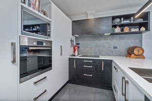 A modern kitchen with built-in appliances, a marble countertop, and a backsplash with a cityscape design. - Endeavour Oasis - Whitianga Holiday Home (Whitianga)