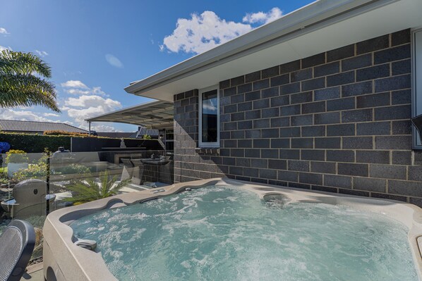 Un espace piscine avec un jacuzzi, une terrasse avec des sièges et une vue sur un bâtiment en briques.