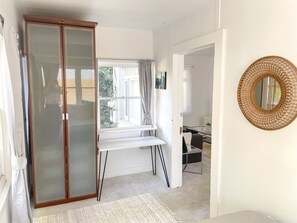 A room with a sliding glass door, a white desk with a chair, a round mirror, and a view of the outdoors. - Charming Victorian Style 3-bedroom house with AC (Santa Monica)