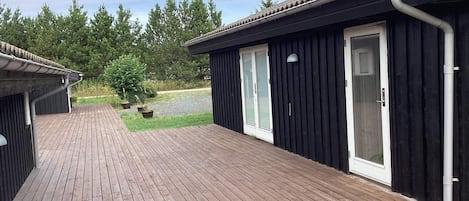 A wooden deck with a black building featuring a sliding glass door.