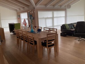 Ein Essbereich mit Holztisch und Stühlen, einer Vase mit Blumen und einer schwarzen Couch im Hintergrund.