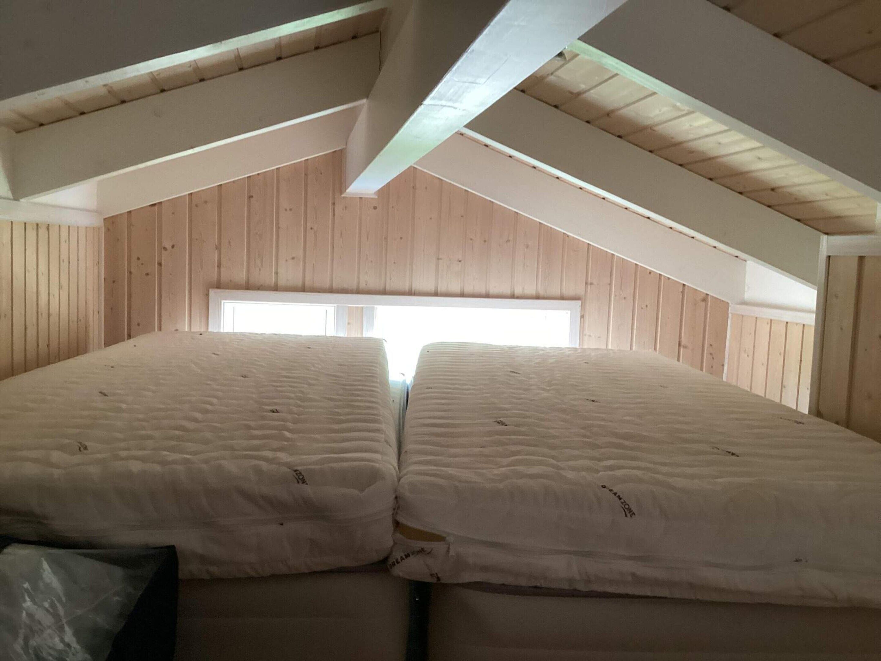 A room with two beds, wooden walls, and a sloped ceiling.