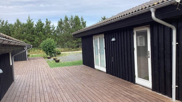 A wooden deck with a black building featuring a sliding glass door. - 4 Star Holiday Home in Jerup (Jerup)