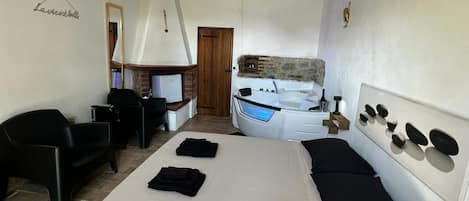 Un dormitorio con una cama grande, un escritorio, una silla, un espejo y un baño con bañera.