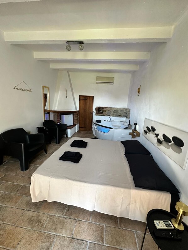 A bedroom with a large bed, a desk, a chair, a mirror, and a bathroom with a bathtub.