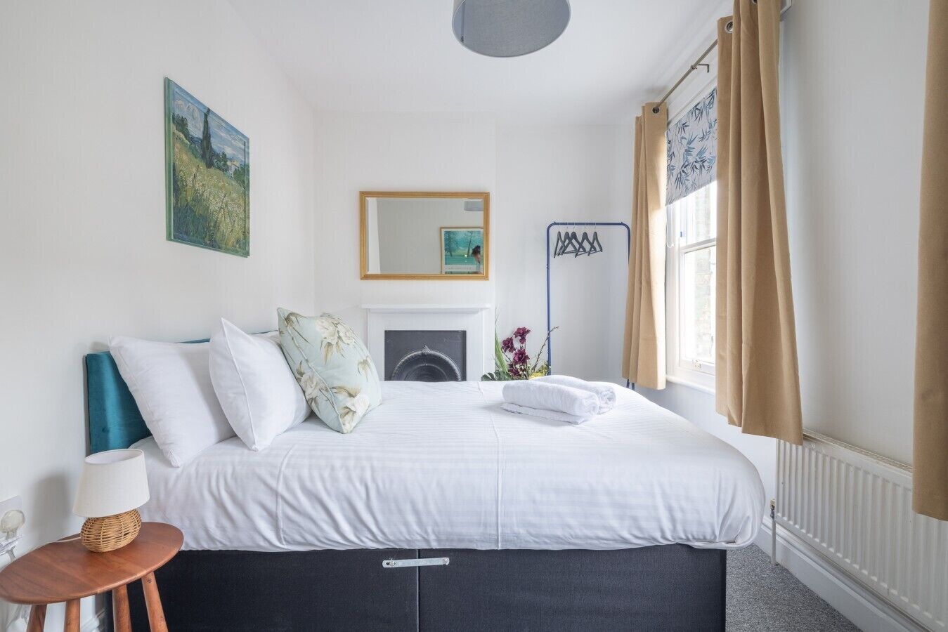 Un dormitorio con cama, mesita de noche con lámpara, espejo y ventana con cortinas.