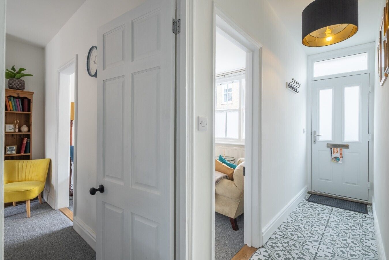 A hallway with a white door, a yellow chair, a bookshelf, and a patterned floor.