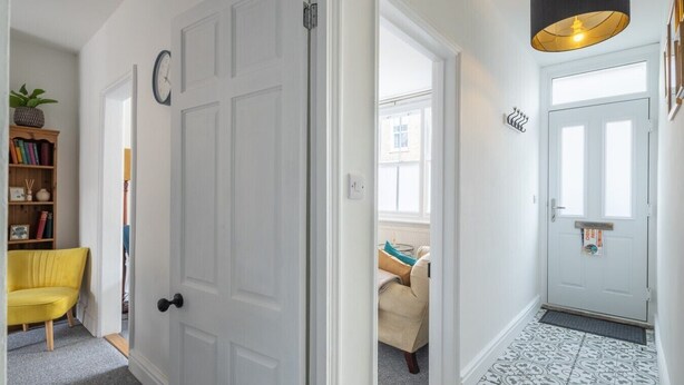 A hallway with a white door, a yellow chair, a bookshelf, and a patterned floor. - Stunning 3Bed Victorian Central Home (Cambridge)