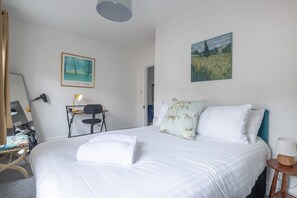 A hotel room with a bed, a desk, a chair, a lamp, a painting, and a mirror. - Stunning 3Bed Victorian Central Home (Cambridge)