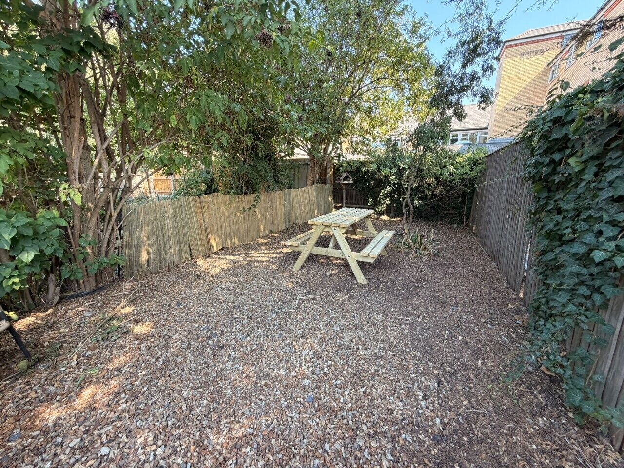 A gravel backyard with a wooden picnic table and a wooden fence.