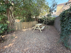 A gravel backyard with a wooden picnic table and a wooden fence. - Stunning 3Bed Victorian Central Home (Cambridge)