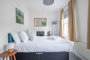 Une chambre à coucher avec un lit, une table de chevet avec une lampe, un miroir et une fenêtre avec des rideaux.