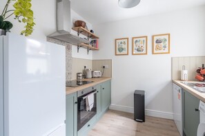 A compact kitchen with a stove, oven, and sink, wooden countertops, and a trash bin. - Charming 3Bed Victorian Home PLUS 1 Bed Annexe (Cambridge)