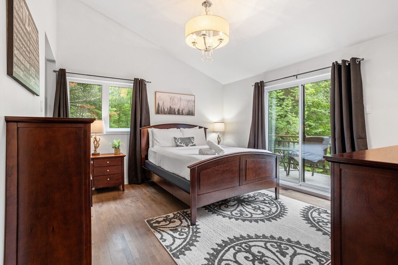 Ein Schlafzimmer mit Bett, Nachttisch, Lampe und Blick ins Freie durch ein großes Fenster.