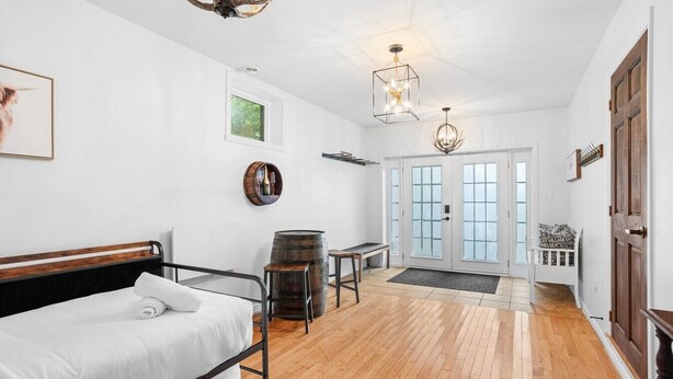 A room with a bed, a wooden floor, a door with glass panels, and a chandelier. - Forest Escape Near Tremblant | Jacuzzi & Arcade (Mont-Tremblant)