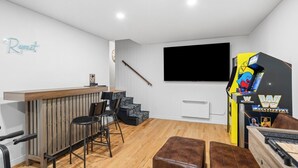 A room with a wooden bar, black chairs, a TV, and a wrestling game machine. - Forest Escape Near Tremblant | Jacuzzi & Arcade (Mont-Tremblant)