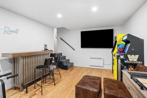 Ein Zimmer mit einer Holztheke, schwarzen Stühlen, einem Fernseher und einer Spielmaschine für Ringen.