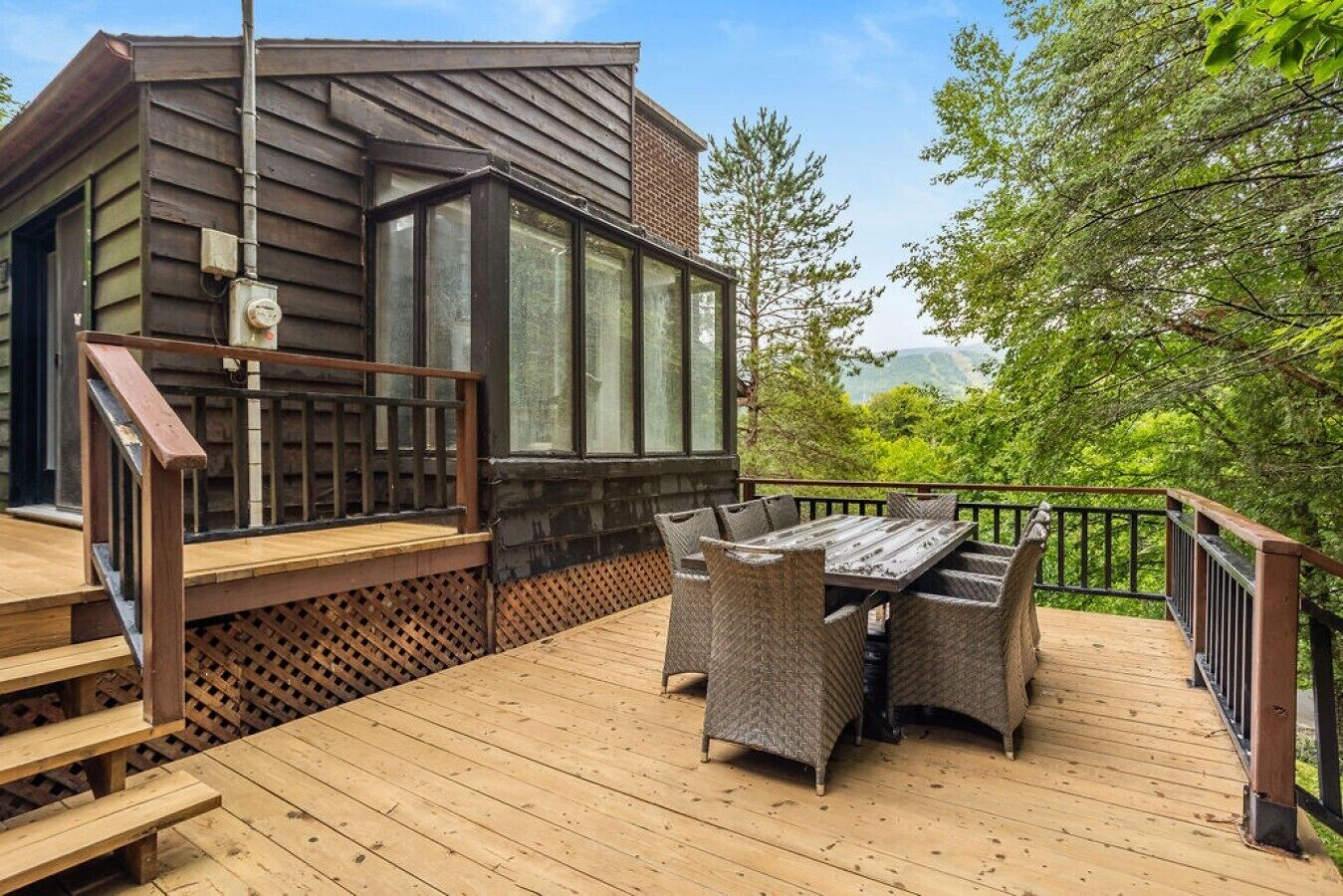 Une terrasse en bois avec une table et des chaises, un escalier et une vue sur la verdure.