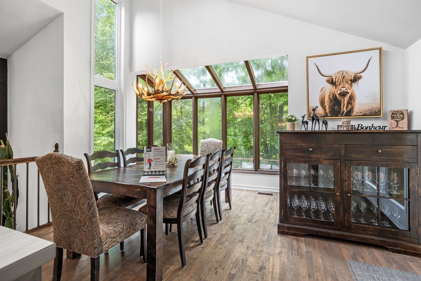 Un coin repas avec une table et des chaises en bois, un lustre et un buffet aux portes vitrées.