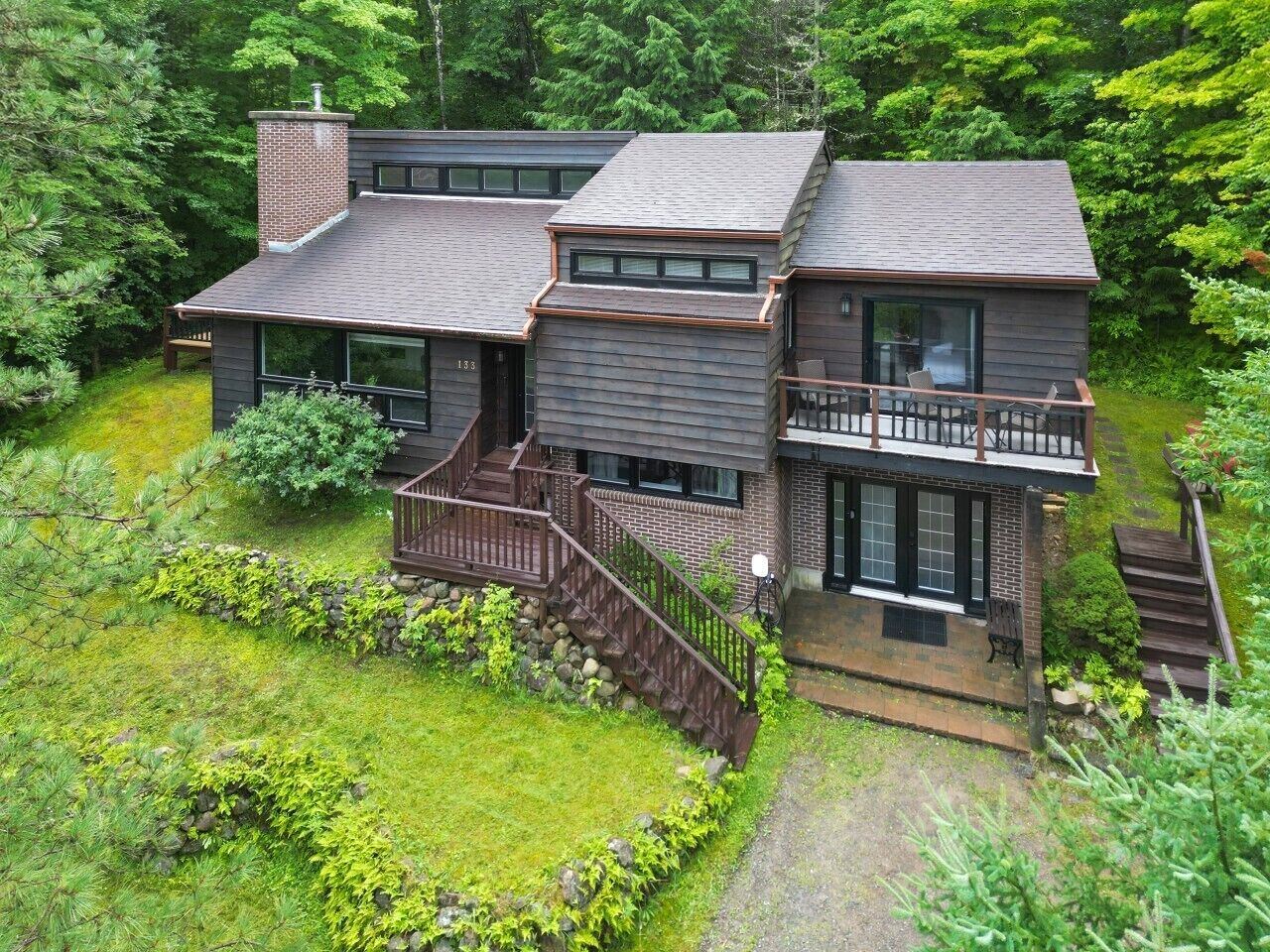 Une maison moderne à deux étages, dotée d’un balcon et entourée d’une végétation luxuriante.