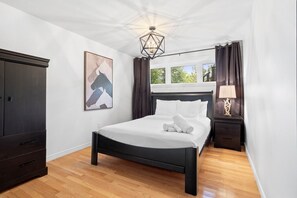 A bedroom with a bed, a nightstand, a wardrobe, a painting, and a window with curtains. - Forest Escape Near Tremblant | Jacuzzi & Arcade (Mont-Tremblant)