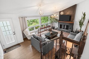 Ein modernes Wohnzimmer mit Kamin, bequemen Sitzmöglichkeiten und einem großen Fenster mit Blick auf Grünflächen.