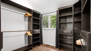 A walk-in closet with multiple shelves and drawers, a wooden hanger rack, and a window with a view of greenery. - Forest Escape Near Tremblant | Jacuzzi & Arcade (Mont-Tremblant)