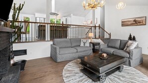 A modern living room with a fireplace, two grey sofas, a coffee table, and a staircase with a railing. - Forest Escape Near Tremblant | Jacuzzi & Arcade (Mont-Tremblant)